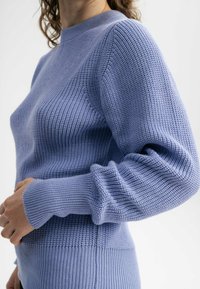 Helles blaues Strickpullover mit einem strukturierten Muster, gerippten Bündchen und Saum sowie einem hohen Kragen. Nahaufnahme, die die Webart des Stoffes zeigt.