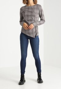 Chemise à manches longues avec un motif à carreaux en gris, rouge et noir. Associée à un jean skinny bleu foncé et des bottines à lacets noires.