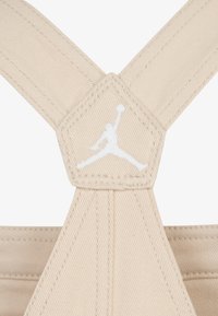 Bežna platnena traka s heksagonalnom naljepnicom na kojoj se nalazi bijeli Jumpman logo. Tekstura se čini glatkom s vidljivim šavovima.