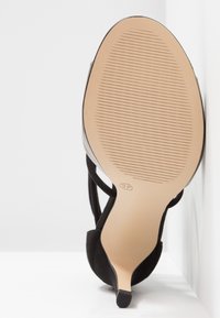 Chaussure à talon haut noire avec une semelle beige lisse, présentant une surface texturée et un bout pointu. Taille indiquée comme 37.