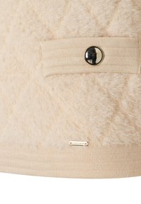 Beige pluizig gebreid stof met een geribde manchette, een glanzende ronde zwarte knop en een klein rechthoekig metalen label aan de onderkant.