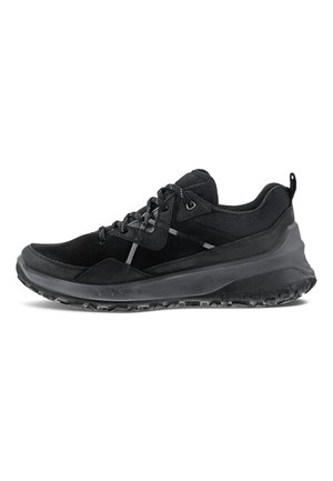 Zapatilla negra de corte bajo con suela gruesa texturizada, parte superior de malla y ante, cierre de cordones y lengüeta en el talón, vista lateral.