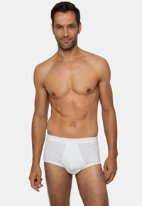 Pantaloni intimi bianchi in cotone con un morbido elastico in vita e una texture a costine, indossati da un uomo con un fisico atletico, in piedi di fronte a uno sfondo semplice.