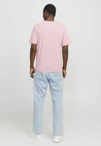 Rosa T-Shirt mit kurzen Ärmeln und Rundhalsausschnitt, kombiniert mit hellblauen weiten Jeans und weißen Sneakers, von hinten betrachtet.