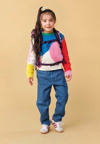 Colorful knit sweater with pink, blue, and yellow accents, paired with loose denim pants and white sneakers with red stripes. Backpack included.