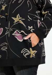 Sweat à capuche noir au fit ample, orné de motifs abstraits en crème, or et violet. Comprend une poche avant et un cordon de serrage au niveau de la capuche.