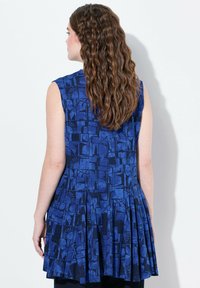 Tunic senza maniche di colore blu con motivo geometrico astratto e design a pieghe svasato. Realizzata in un tessuto morbido e liscio.
