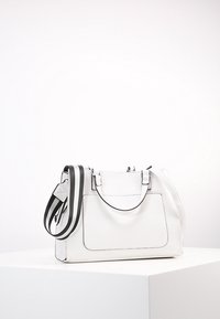 Sac à main blanc texturé avec sangle d'épaule rayée noire, double poignées et une poche avant. Caractérisé par une quincaillerie argentée et des lignes épurées.