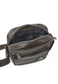 Bolsa mensajera de cuero marrón con un compartimento principal con cremallera. El interior cuenta con un forro impreso y una correa de hombro de tela ajustable.