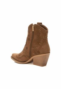 Bota de tobillo de ante marrón con cremallera lateral, acentos de tachuelas, punta afilada y tacón apilado. Presenta costuras decorativas y patrones de estrellas.