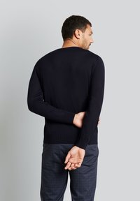 Marineblauer Langarmpullover aus glattem Strickstoff, mit Rundhalskragen und geripptem Saum, getragen mit gemusterten Hosen.