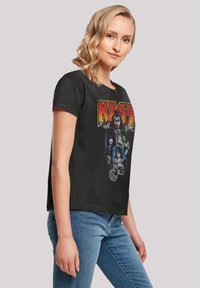 Black cropped t-shirt featuring a colorful graphic print of four musicians and the "KISS" logo in bold, yellow letters. Cotton material.
