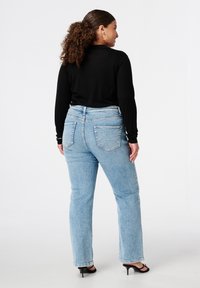 Lichtblauwe denim jeans met een rechte pijp, voorzien van een gematigde taillehoogte, riemlussen, zichtbare stiksels en achterzakken. Ggedragen met een zwart top.