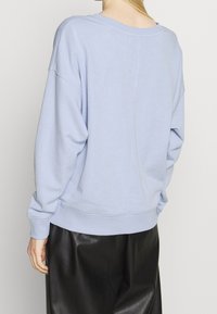 Sudadera azul claro con un corte holgado, costuras de hombro caídas, puños y dobladillo acanalados, combinada con pantalones negros de cuero sintético.