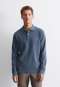 Mouwloze polo in gedempt blauw katoen, met een knoopsluiting bij de kraag, een subtiele logo op de linkerborst en geribbelde manchetten.