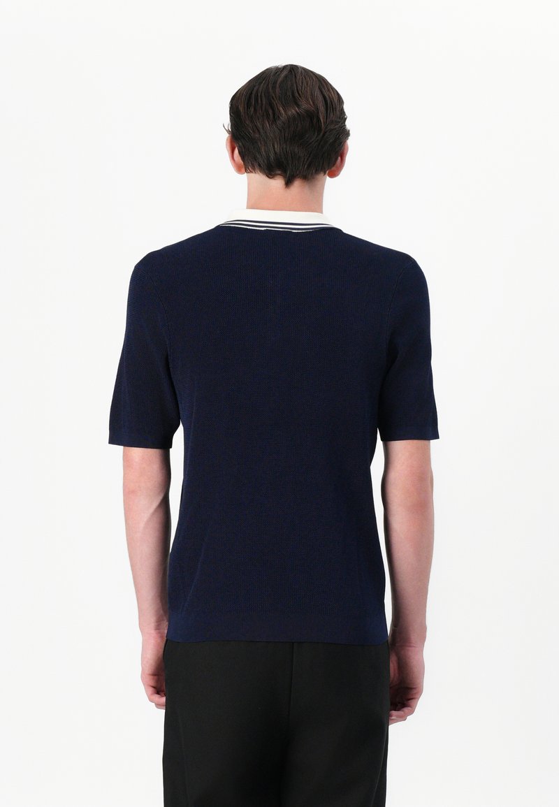 Marineblauer Kurzarmpullover mit rippierter Textur, ausgestattet mit einem kontrastierenden, weiß gestreiften Kragen und einer taillierten Passform. Minimalistischer Stil, keine sichtbaren Logos.