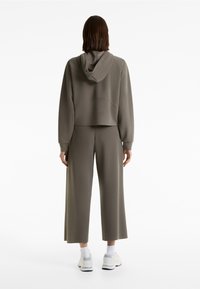 Dunkelgrüner, kürzer geschnittener Kapuzenpulli mit Kapuze und langen Ärmeln, kombiniert mit weit geschnittenen Hosen in passender Farbe. Glatte Textur, minimalistisches Design.
