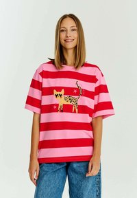 Růžové a červené pruhované tričko s grafikou kočky s leopardím vzorem a hvězdnými akcenty. Volný střih a krátké rukávy, vyrobené z měkké tkaniny.