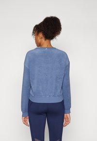 Blaues Fleece-Sweatshirt mit gerippten Bündchen und Saum. Weicher Stoff, runder Halsausschnitt und leicht verkürzte Passform. Kombiniert mit dunklen Leggings.
