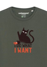 Groene katoenen T-shirt met een zwart kattenafbeelding met witte ogen en een rode accent, met de tekst "IK DOE WAT IK WIL" eronder.