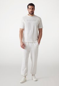 Hvid bomulds t-shirt med et subtilt tekstureret logo, parret med hvide sweatpants med elastiske manchetter og et lille logo detalje på benet.