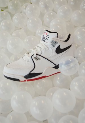 Biało-czarny sneaker Nike Air Flight spoczywający na łóżku z przezroczystych białych plastikowych kulek.