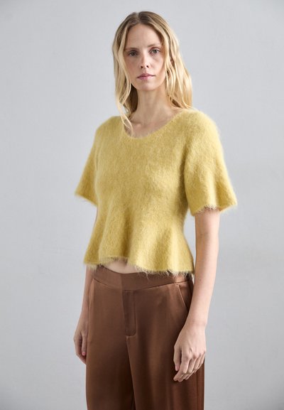 Maglioncino giallo e peloso con maniche corte e scollatura ampia, abbinato a pantaloni in satin marroni. Texture morbida e vestibilità ampia.