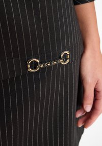 Zwarte stof met krijtstrepen, voorzien van een metalen kettingdetail met ronde schakels, die een gladde textuur en een tailored ontwerp laat zien.