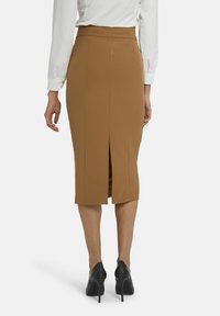 Jupe crayon marron avec une fente à l'arrière, en tissu texturé, assortie à des chaussures à talons noirs. Vue de derrière.
