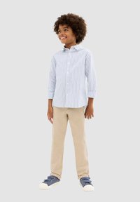 Chemise boutonnée rayée bleu clair et blanche à manches longues, pantalon beige et baskets marines avec semelles blanches. Design simple et décontracté.
