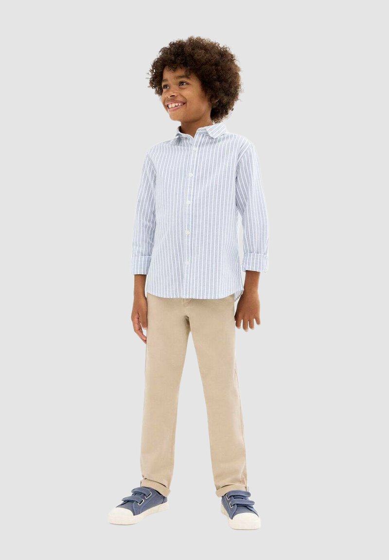 Chemise boutonnée rayée bleu clair et blanche à manches longues, pantalon beige et baskets marines avec semelles blanches. Design simple et décontracté.
