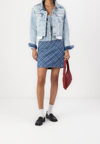 Ljusblå jeansjacka med fransiga kanter, knäppt framtill, kombinerad med en blå rutig kjol. Svarta loafers och röd handväska fulländar utseendet.