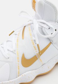 Sneakers Nike blanches avec un dessus en mesh, des accents dorés, le texte "Just Do It", des détails en cuir lisse et une semelle mouchetée.