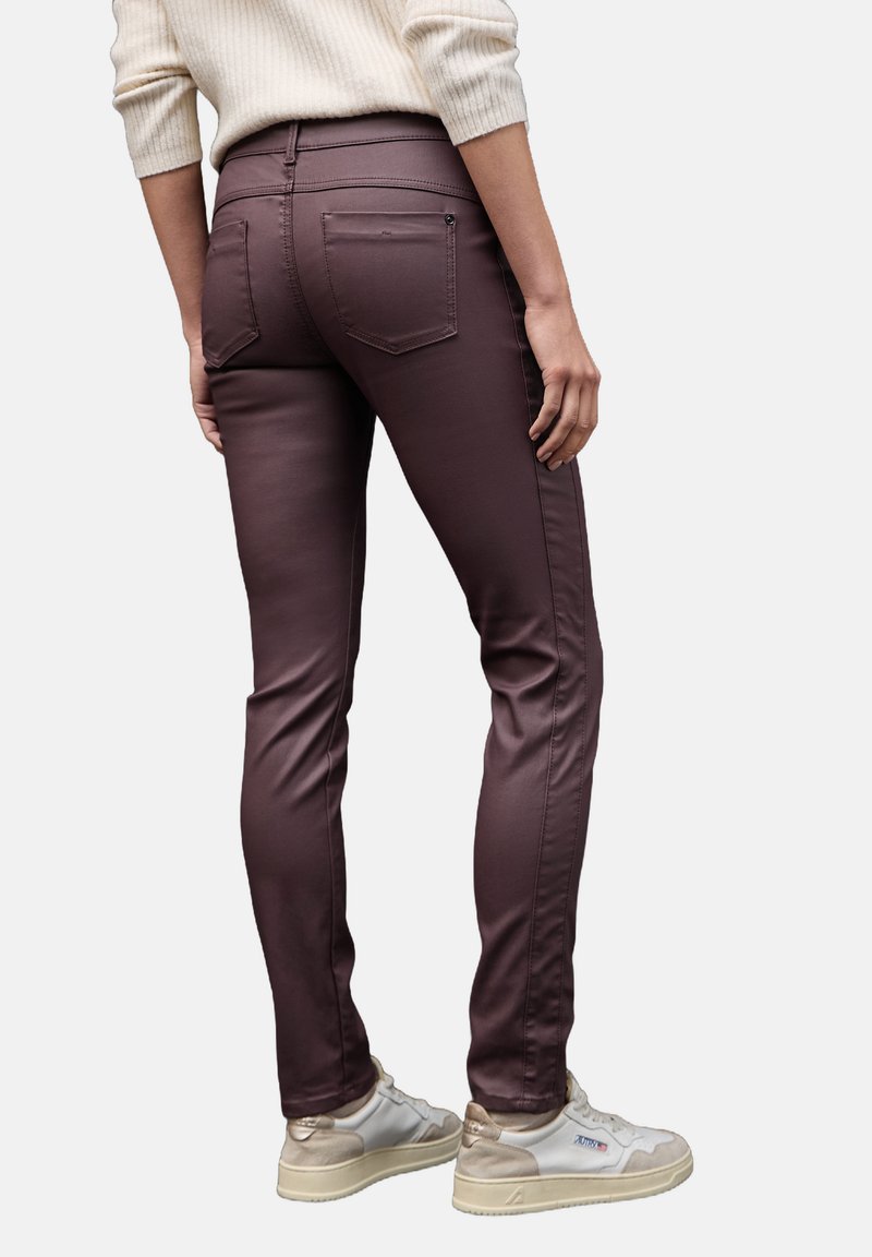 Bordeaux stretch jeans met slim fit, hoge taille, achterzakken en naaddetails, gecombineerd met witte en beige sneakers.