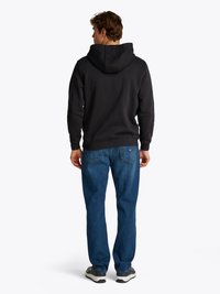 Sweat à capuche noir avec cordon de serrage, associé à un jean bleu et des baskets grises, vu de dos.