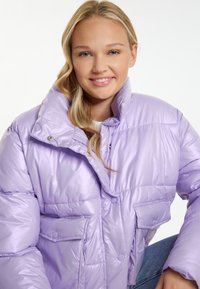 Giacca puffer lavanda con colletto alto, bottoni frontali e due tasche laterali. Il materiale è lucido e trapuntato per un tocco di texture in più.