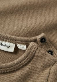 Nahaufnahme eines braunen Strickbabykleids mit Druckknöpfen in der Nähe des Kragens und einem Etikett, das die Größe 1-2 Monate zeigt.