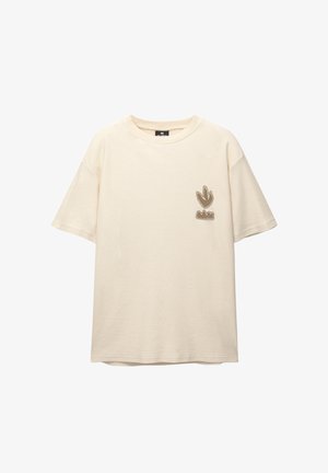 Lyhythihainen kerma värinen t-paita puuvillasta, jossa on ribbitekstuuri. Vasemmassa rinta-alueessa on ruskea brodeerattu logo.