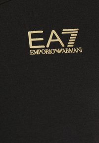 Černý tričko z látky s žebrovanou strukturou, na němž se nachází výrazně umístěné zlaté potisk logo "EA7 EMPORIO ARMANI".