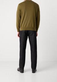 Pull en tricot vert olive avec poignets et ourlet côtelés, associé à un pantalon texturé gris foncé et des chaussures noires, vu de dos.