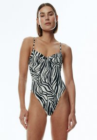Einteiliger Badeanzug mit schwarz-weißem Zebra-Muster, dünnen verstellbaren Trägern und einem hochgeschnittenen Beinausschnitt. Glatte, elastische Stoffoberfläche.