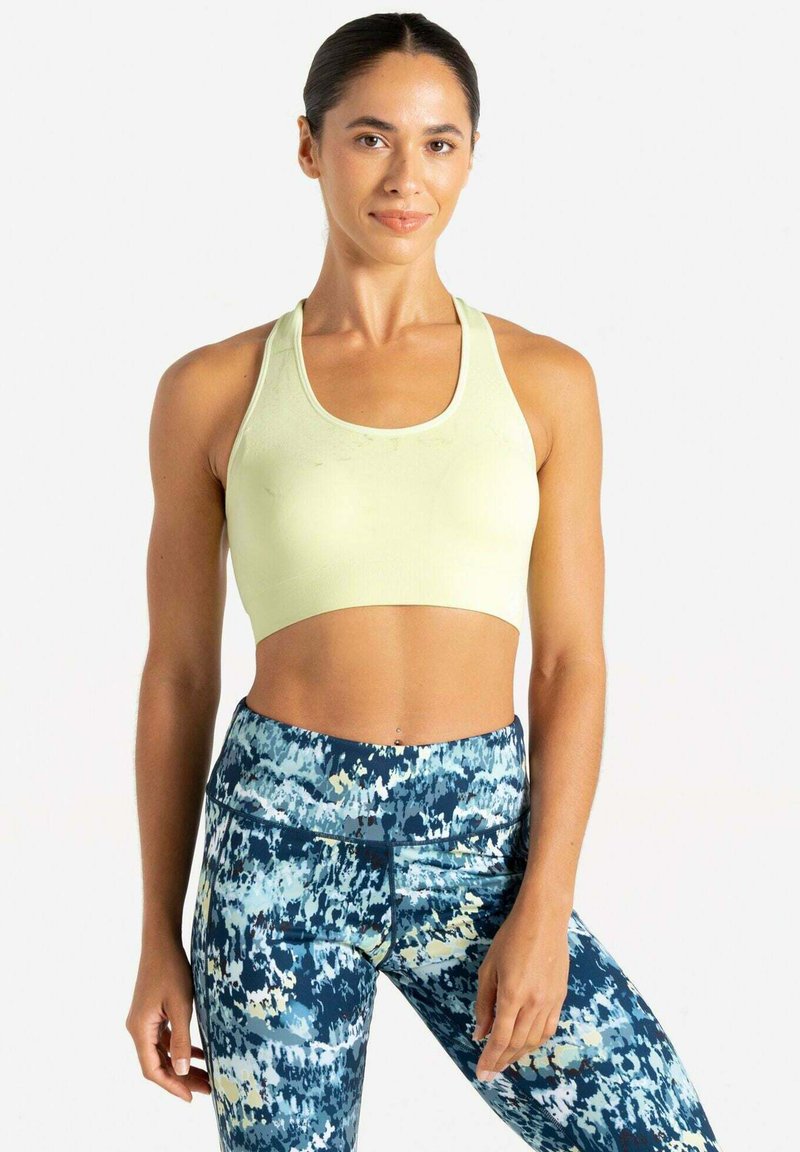 Hellgrüner Sport-BH mit Rundhalsausschnitt. Kombiniert mit blauen Leggings mit Mustern, die abstrakte Designs in Weiß- und Gelbtönen zeigen.