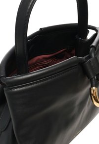 Sac à main en cuir noir doté d'une texture lisse, d'un accastillage en or et d'un intérieur en tissu rouge avec une poche zippée.