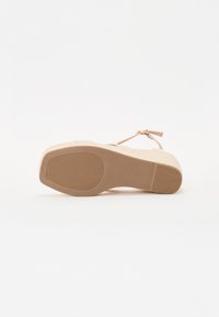 Platåsandaler med en strukturert beige såle, tynn ankelrem og rund tå med minimale metalldetaljer og en glatt overflate.