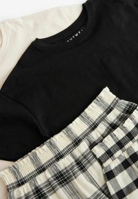 Due t-shirt di cotone, una nera e una beige, sovrapposte a leggere pantaloni da pigiama a scacchi in crema e nero con una cintura elastica.