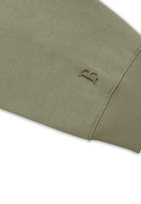 Sudadera verde oliva con puños acanalados y un sutil detalle de logo bordado. Textura suave, diseño casual, enfocado en la comodidad y la usabilidad.
