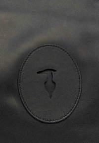 Černý kožený materiál s hladkým povrchem. V centru se nachází kulatý embosovaný logo s vyřezávaným designem. Subtilní švy.