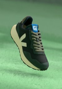 Dark green sneaker with light green accents, textured fabric, and a blue logo tag. Features a cushioned sole and rounded shape.