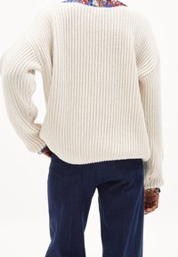 Maglione a maglia color crema con texture a coste, vestibilità oversize e spalle scese, abbinato a jeans blu scuro. Mostra la vista posteriore.