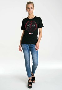 Black cotton t-shirt with a red and gray graphic design, round neckline, worn with light blue jeans and black platform sandals.